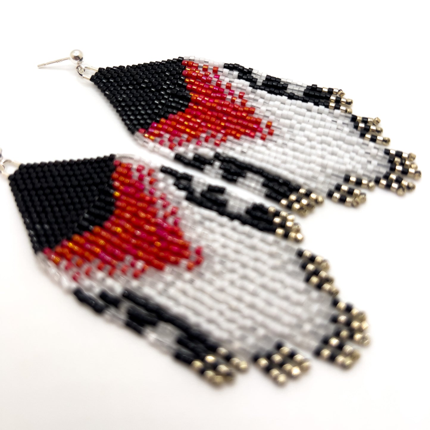 Close up of Rose Breasted Grosbeak inspired earrings on a white background, showcasing a bold rose and white design against a black base, leading into a layered fringe of black, white, and clear beads.