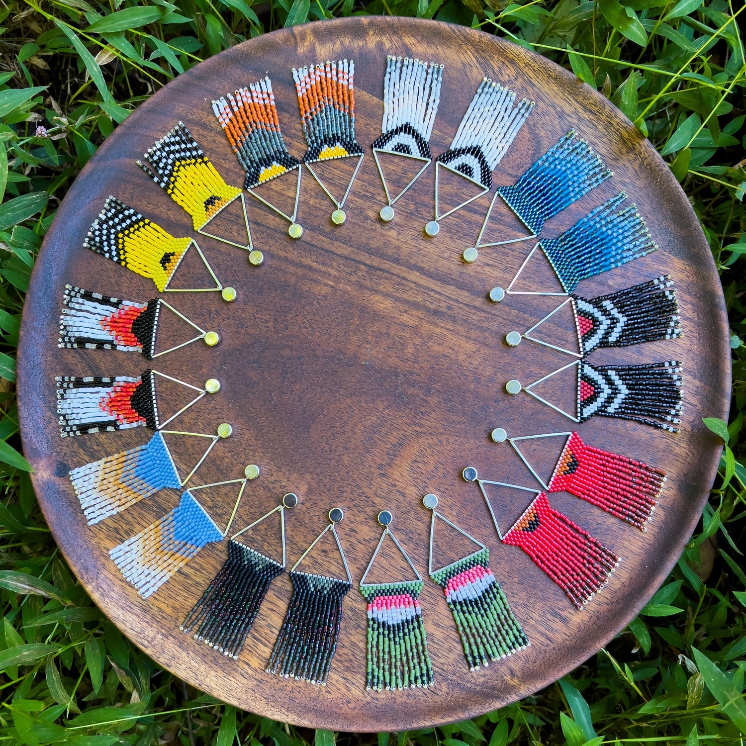 A wooden tray filled with an array of colorful bird-themed beaded earrings, arranged in a circle, capturing the vibrant patterns of different bird species.