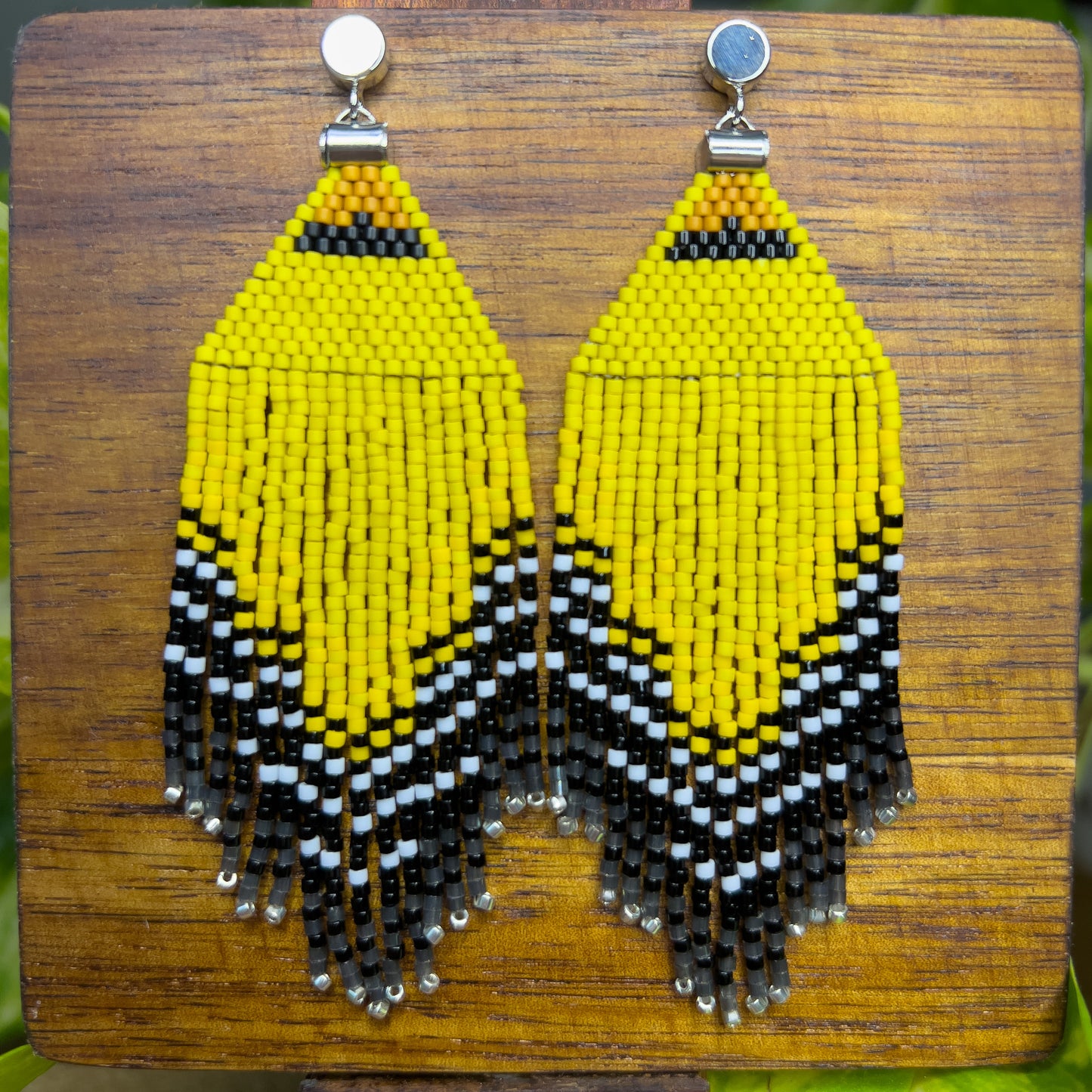 American Goldfinch-inspired handcrafted beaded earrings displayed on a wooden surface, showcasing bright yellow, black, and white patterns with fringe detail.