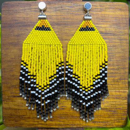 American Goldfinch-inspired handcrafted beaded earrings displayed on a wooden surface, showcasing bright yellow, black, and white patterns with fringe detail.