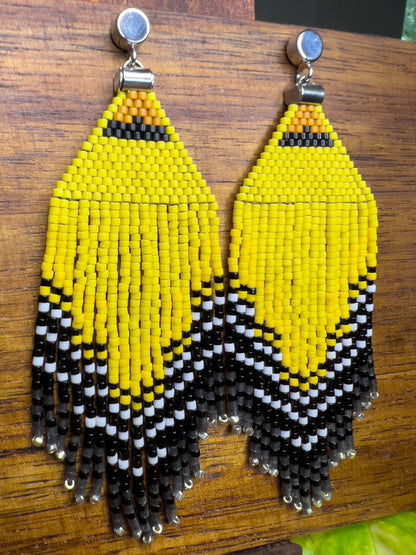 Side view of American Goldfinch-inspired handcrafted beaded earrings displayed on a wooden surface, showcasing bright yellow, black, and white patterns with fringe detail.