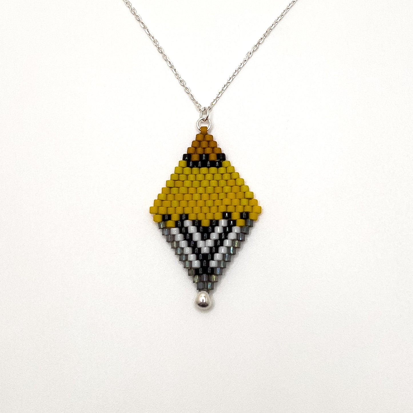 Close up of American Goldfinch-inspired handcrafted beaded pendant with a sterling silver chain displayed on white surface, showcasing bright yellow, black, and white pattern.
