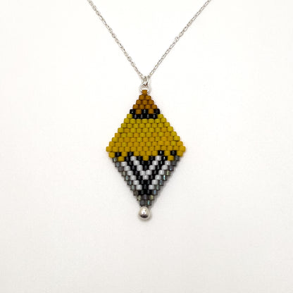 Close up of American Goldfinch-inspired handcrafted beaded pendant with a sterling silver chain displayed on white surface, showcasing bright yellow, black, and white pattern.