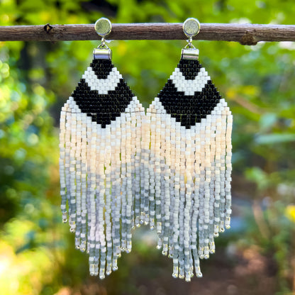 Carolina Chickadee inspired beaded earrings hanging in a natural setting, featuring a bold black and white V-shape at the top that resembles the bird’s distinctive head pattern, followed by soft cream and gray fringe 