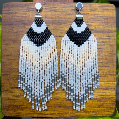 Carolina Chickadee inspired beaded earrings on a wooden background, featuring a bold black and white V-shape at the top that resembles the bird’s distinctive head pattern, followed by soft cream and gray fringe.