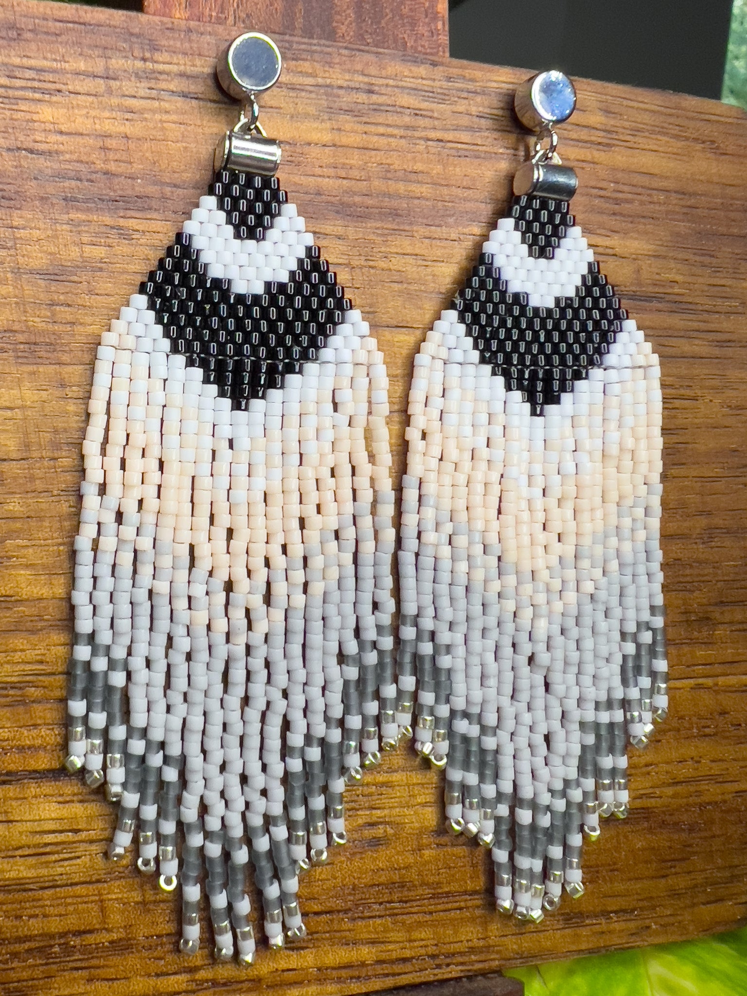 Side view of Carolina Chickadee inspired beaded earrings on a wooden background, featuring a bold black and white V-shape at the top that resembles the bird’s distinctive head pattern, followed by soft cream and gray fringe.