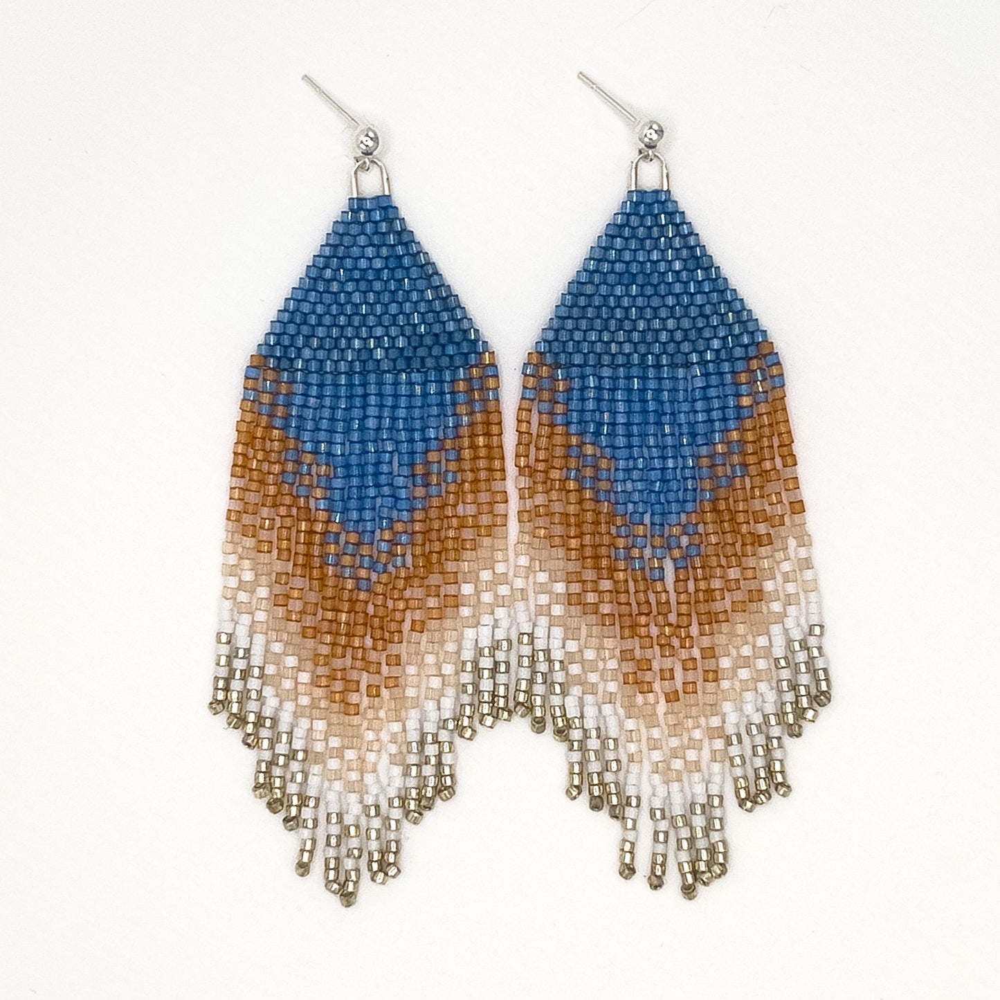 Pair of beaded Eastern Bluebird earrings laying on a white background, featuring a vibrant blue triangular top with layered amber and white beaded fringe, creating a gradient effect from deep blue to warm amber and soft white.