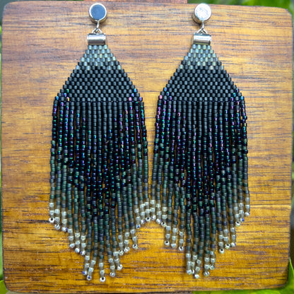 European Starling inspired earrings on a wooden background, showcasing a deep black beaded section that fades into iridescent fringe with hints of green and purple.