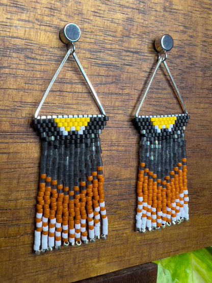 Side view of handcrafted beaded earrings inspired by an American Robin displayed on a wooden surface, showcasing a triangular design with yellow, black, orange, and white beads in a vibrant, nature-inspired pattern.