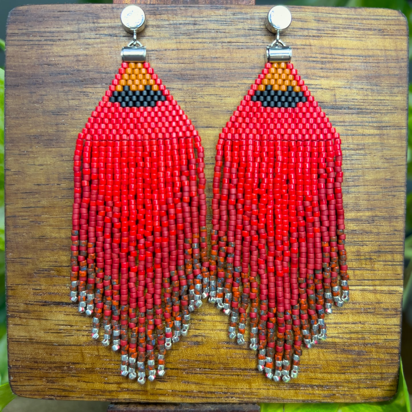 Vibrant red beaded Northern Cardinal earrings on a wooden background, showcasing an orange and black beaded section at the top, followed by cascading red fringe that fades into subtle silver bead accents at the bottom.