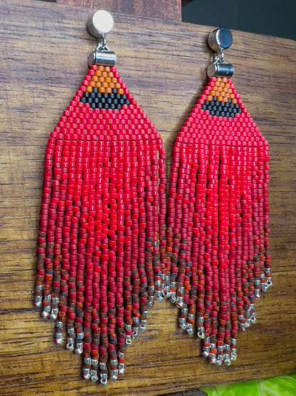 Side view of vibrant red beaded Northern Cardinal earrings on a wooden background, showcasing an orange and black beaded section at the top, followed by cascading red fringe that fades into subtle silver bead accents at the bottom.