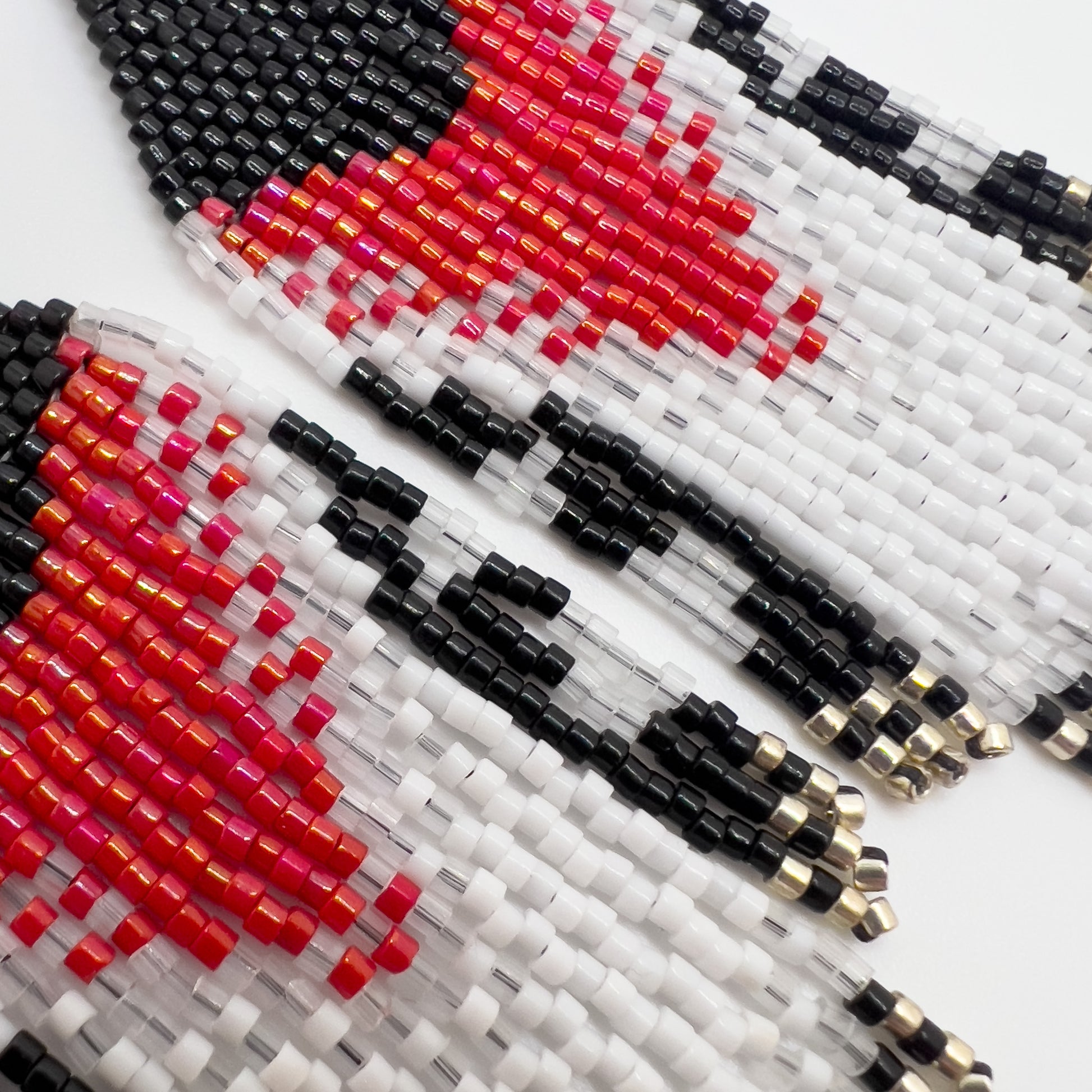 Close up of Rose Breasted Grosbeak inspired earrings on a white background, showcasing a bold rose and white design against a black base, leading into a layered fringe of black, white, and clear beads.